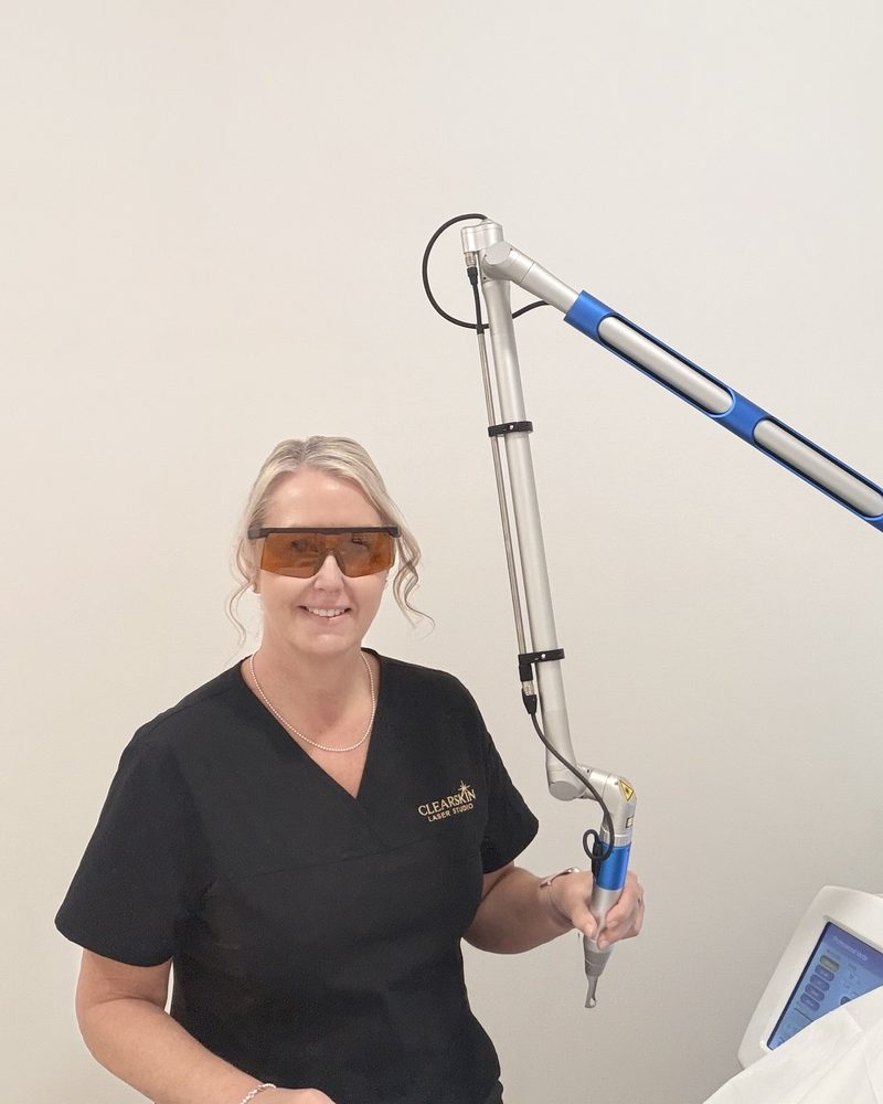 Sandi smiling beside the Spectrum Quattro laser in the Oxenford studio